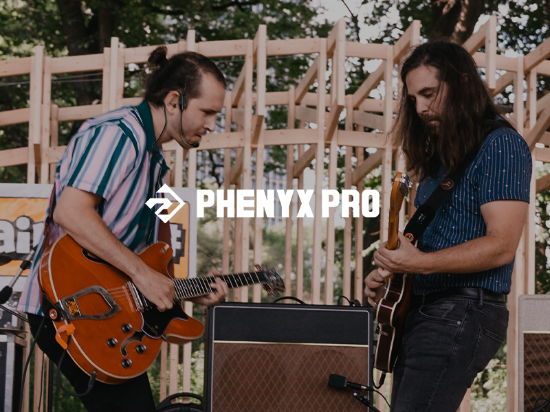 Musicians performing outdoors with electric guitars, one orange guitar visible. Stage equipment includes an amplifier. PHENYX PRO branding visible.