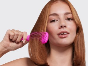 A woman brushing her hair with a pink ultimate detangler brush.