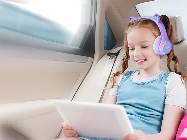 Purple cat-ear shaped wireless headphones worn by a child using a tablet device in a vehicle. Headphones feature LED lights on ear cups.