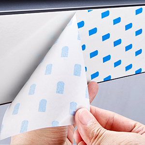 Close-up demonstration of peeling back a white surface material revealing blue diamond pattern underneath.