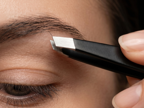 Close-up of eyebrow grooming being performed with black handheld precision tool against person's eye area and brow.