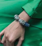 Close-up of a wrist wearing multiple bracelets against a bright green background. Bracelets appear to be beaded or jeweled.