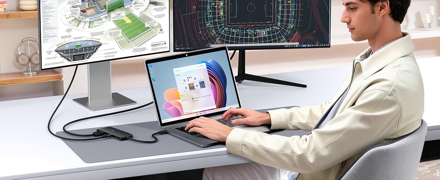 Person working at desk with laptop and digital display screen showing professional workspace setup. Multiple monitors and technology devices visible.