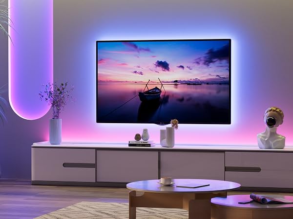 Large flat-screen TV with ambient backlighting displaying sunset scene. TV mounted above white cabinet in modern living room with purple-tinted lighting and decorative items.