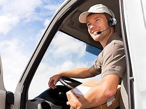 Person wearing a headset and cap, sitting in the driver's seat of a vehicle, looking out the window with a smile.