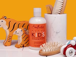 SheaMoisture Kids Shampoo bottle with shower accessories and soap against orange background.