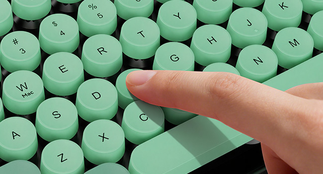 Close-up of Green Black keyboard with round white keycaps being pressed by a finger.