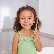 Beautiful young girl with a bright smile holding an Auromere Bamboo Toothbrush