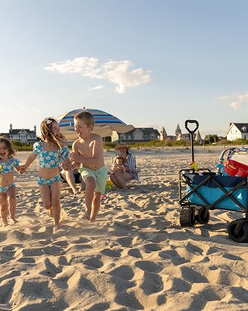 kids running in sand at beach. beach cart with toys. dunes and houses in backgorund
