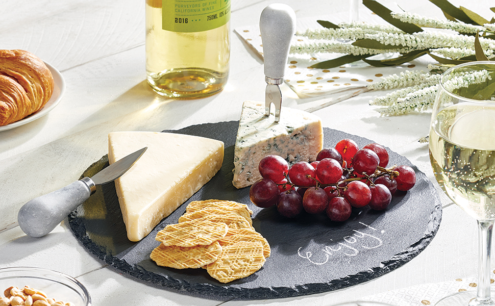 slate stone platter tray holding crackers, grapes, cheese, knives on a white wood table, wine, glass