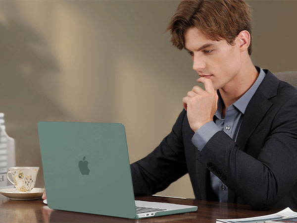 Green Apple MacBook laptop on desk with person in suit jacket using it. Coffee cup and papers visible on table.