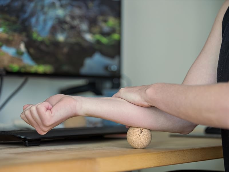 person massaging their forearm at a desk with a rawlogy cork massage ball