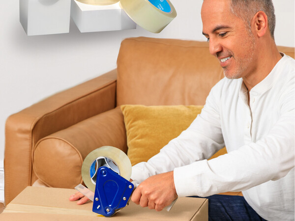 A smiling man tapes a box closed in his living room with Spartan Industrial’s clear packing tape