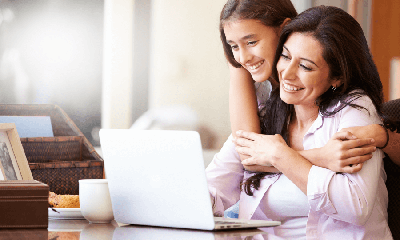 A girl is putting her arms around a woman while they are watching someing on the laptop