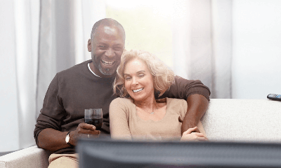 A man is putting his arms around a woman while they are watching someing on TV