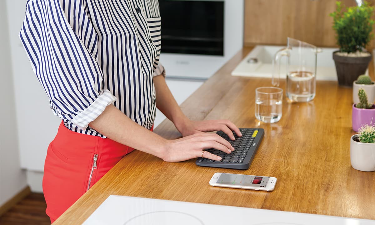 a woman typing on Logitech K380 keyboard placed on a wooden desk