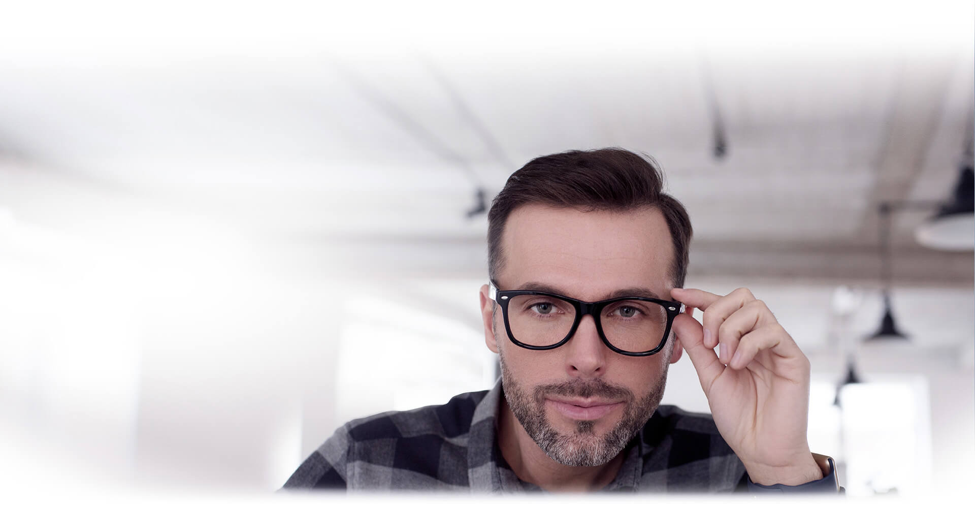 A man touching the brim of his glasses looking towards the vieweer