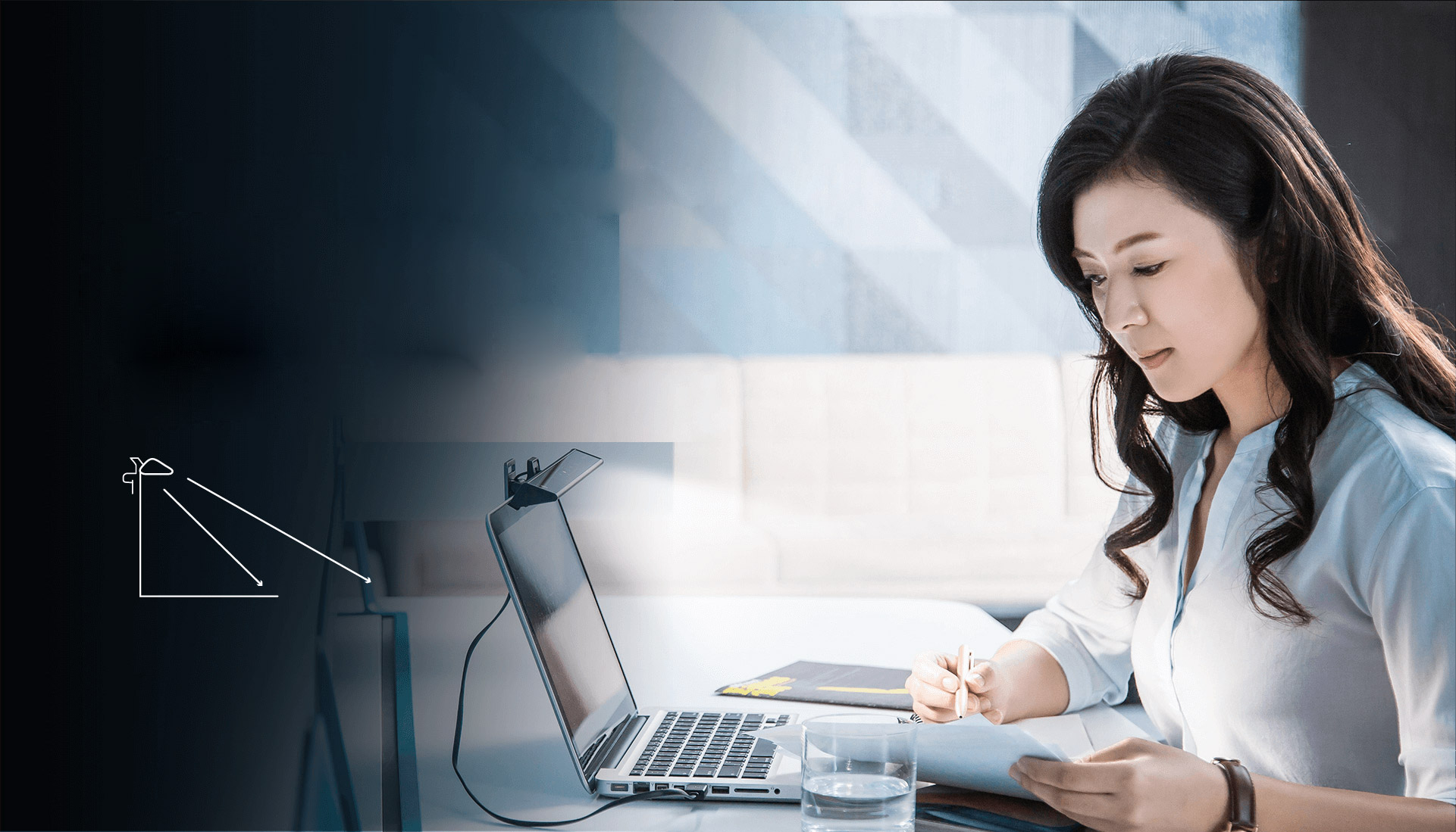 A female office worker taking notes next to her open laptop that has a mounted BenQ ScreenBar Lite