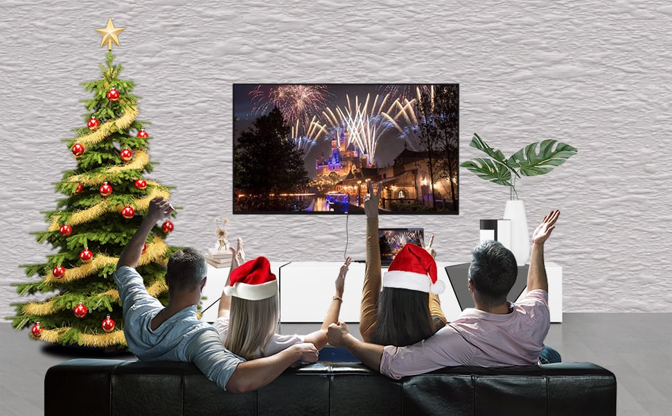 Two male-female couples watching TV that's connected to a laptop, next to a Christmas trees, the two women are wearing santa heats