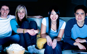 Two couples on a couch next to a bowl of popcorn watching something at night