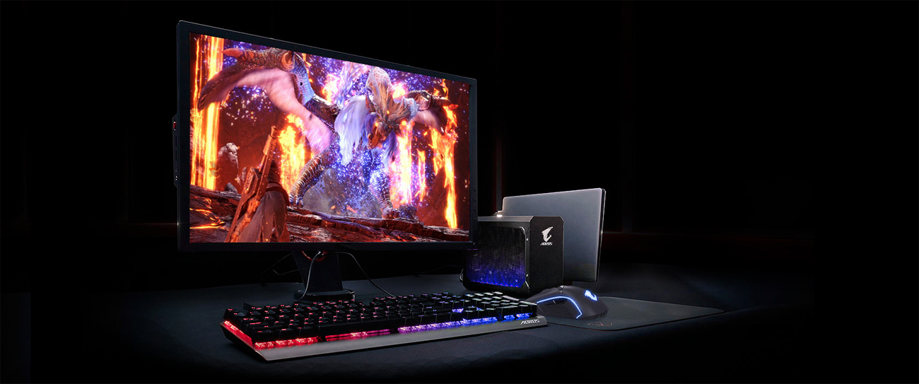 A gaming setup with the external graphics card connected to a laptop, a monitor showing a dragon in fiery domain and a keyboard + mouse