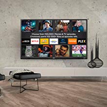 The TV mounted on a wall next to various house items like vases and cushioned seat