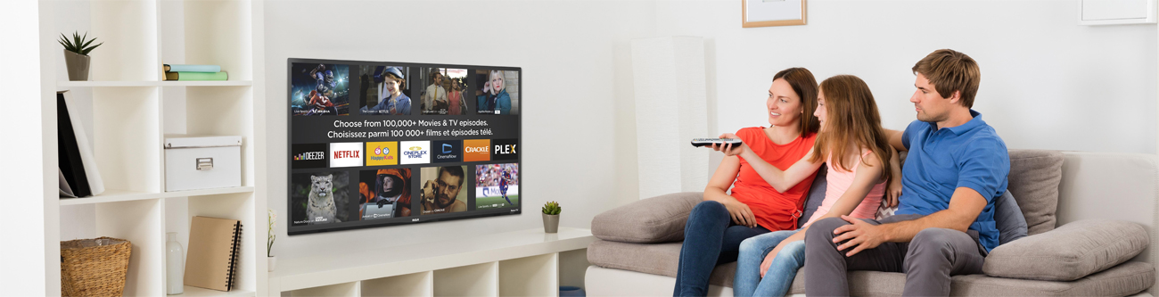 A family of three (mother, daughter and father) sitting on a couch navigating the Roku TV home screen on a mounted RTRU5028-CA TV in their living room