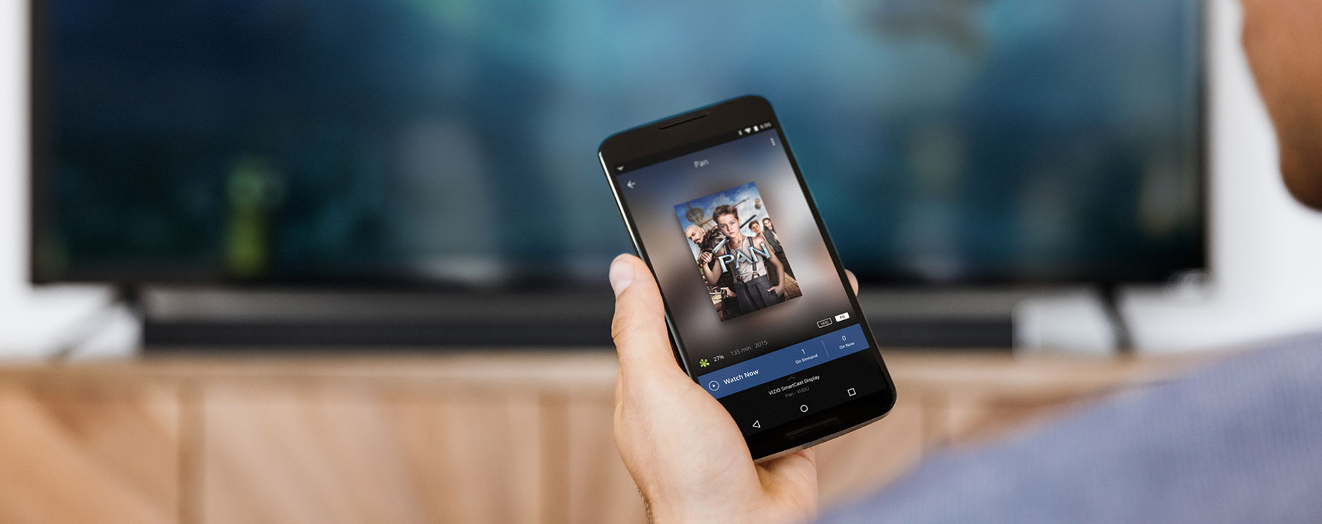 A man in his living room looking down at his smartphone, with the movie 'Pan' getting ready to be played