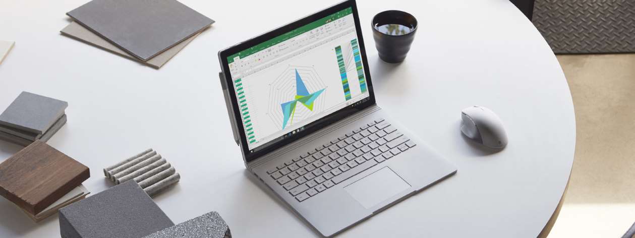  A Surface Book 2 on display on a round table, with a wireless mouse, a cup of tea, some notebooks around this laptop  