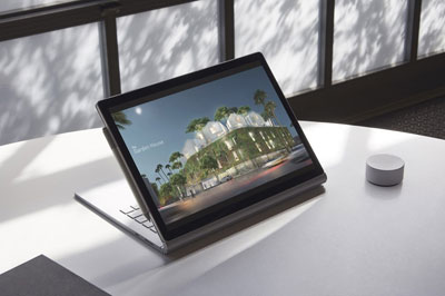  A Surface Book 2 attached to the keyboard and positioned in Stand mode, on a round table. A Surface Pen attached to the side of the screen, and a Surface Dial is to the right of the Surface Book 2 on the table  