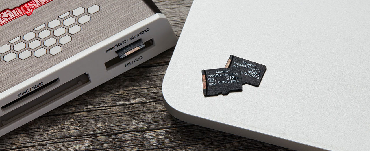  A 256GB card and a 512GB card on top of a laptop cover. Next to them on the right is a multi-card reader with a microSD card in the slot 
