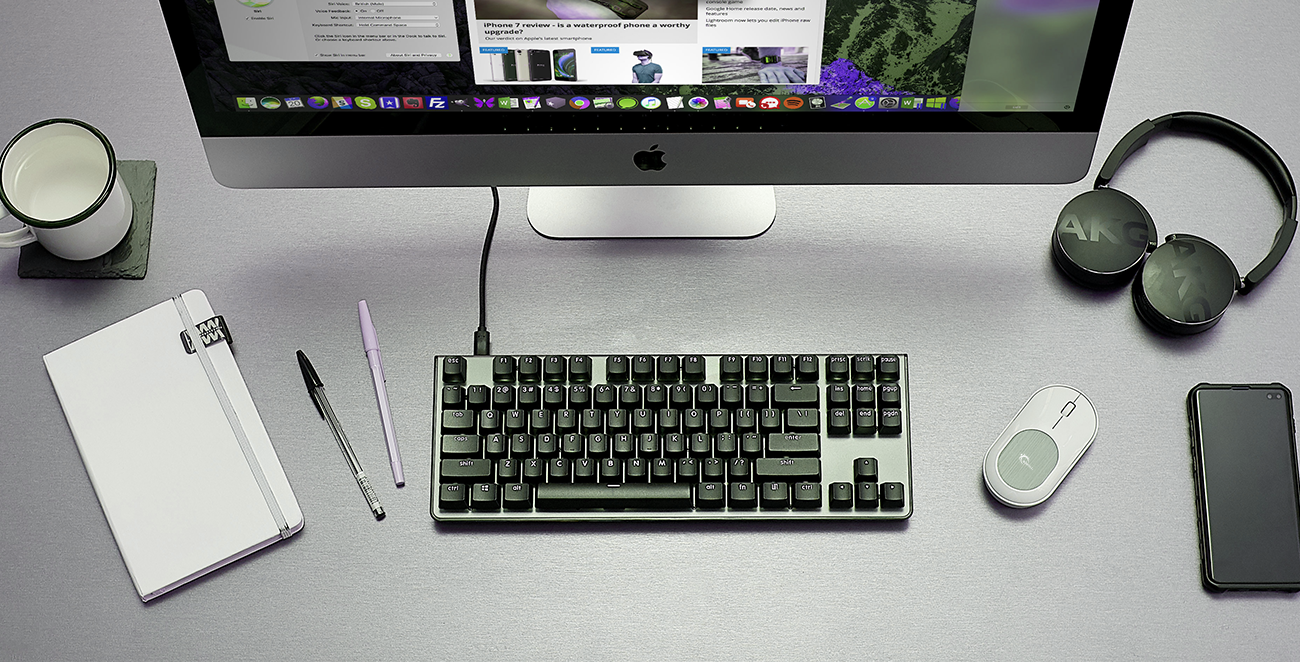 a desktop with a computer, a black keyboard, a mouse, a phone , a cup of water, a notebook, a headphone and two ballpens 