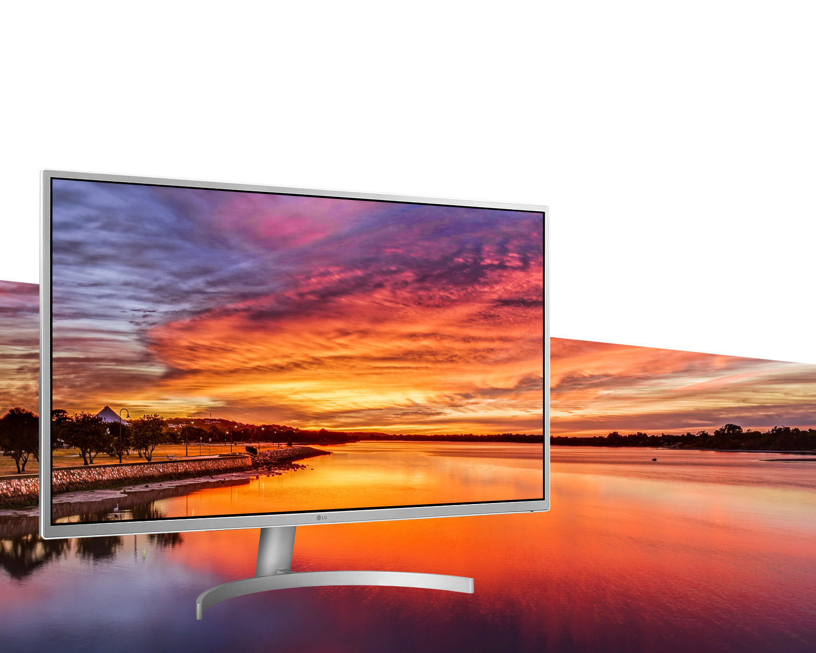 The LG 32QK500-W monitor showing an image of a lake during orange dusk twilight, the image continues as the background of the entire banner
