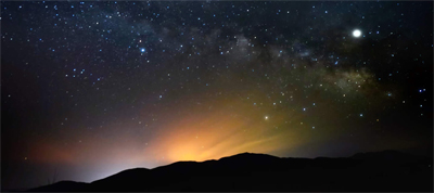 Night time lights and stars in the sky over a dark mountain range