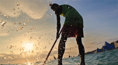 A paddler boarder in the ocean at twilight hour, wearing a helmet that has the Osmo Action attached
