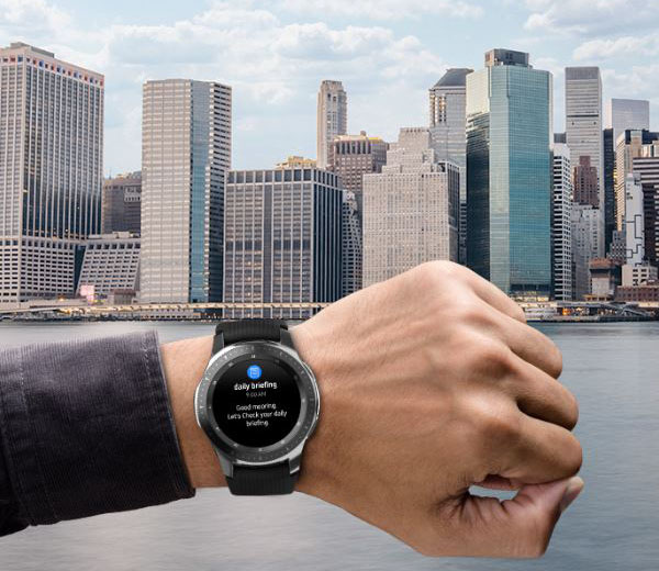 A hand with a watch on is raised up during daytime against a backdrop of skyscrapers