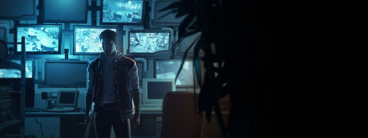 A young man stands in front of a wall of lit up monitors. 