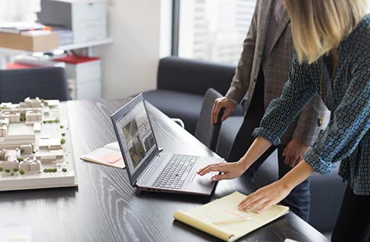 Two People Looking and Using an Open Laptop on a Desk