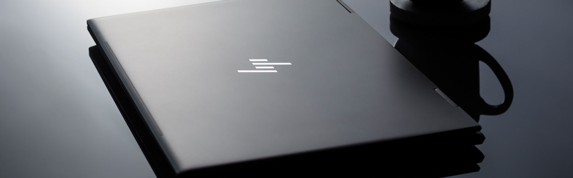 Closed HP ENVY Laptop Next to a Coffee Mug on a Glass Surface