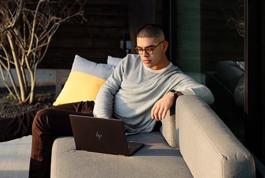 A man outside on a couch browsing through his open HP ENVY laptop