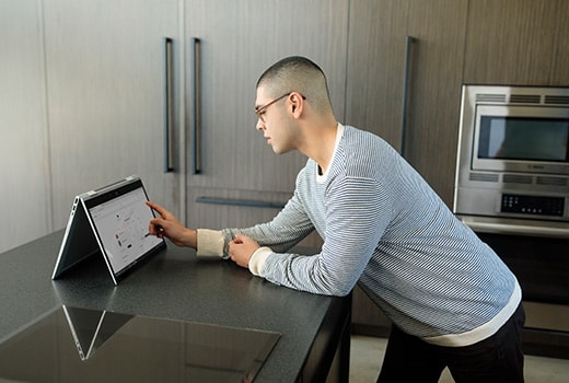 A man touching an HP ENVY that's in tent mode on his kitchen island counter