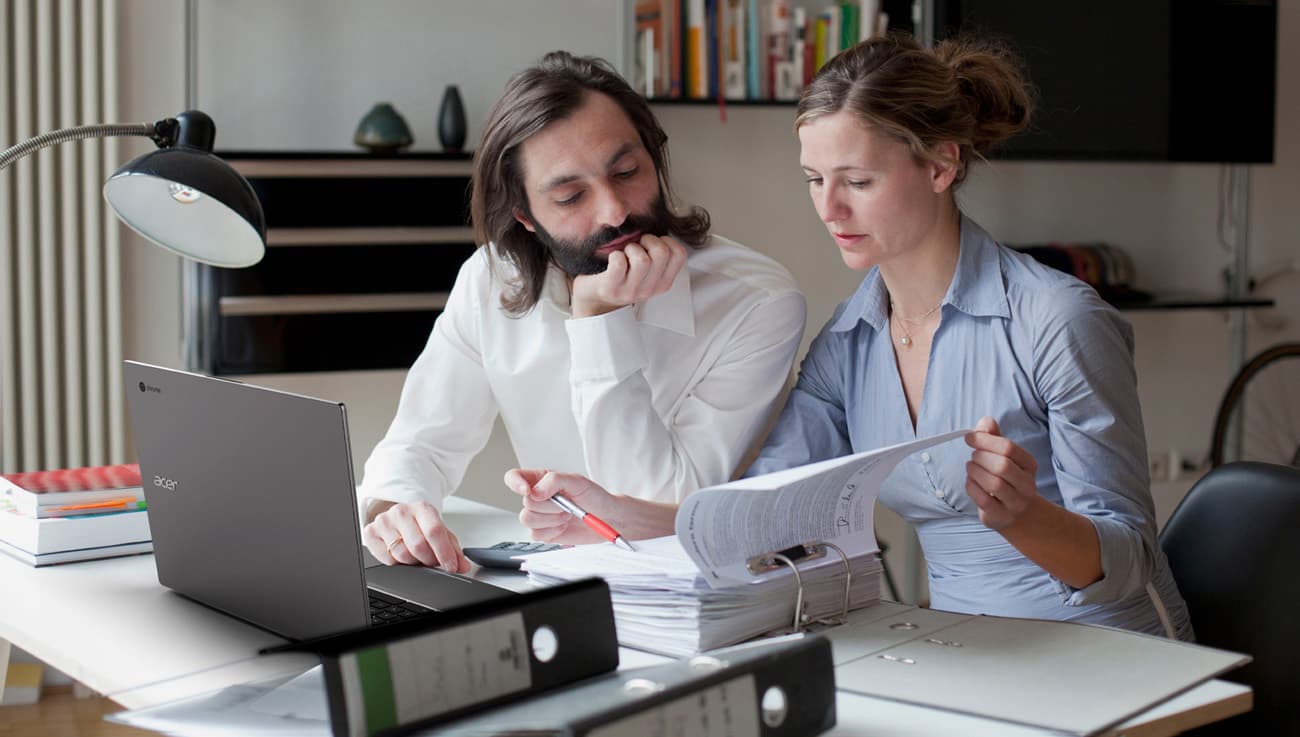 a man and a woman are reading documents with Acer Chromebook 715 in front of them