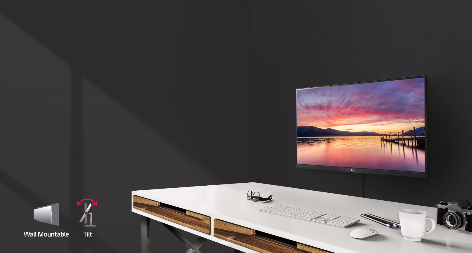 A wall-mounted LED 22MK600M-B monitor in front of a desk that has glasses, a keyboard, mouse cup, camera and pencils