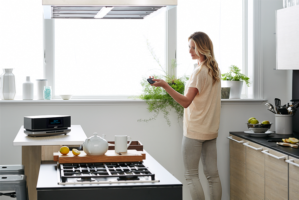 A bose music system IV in the kitchen area where a woman is tending to her house plants