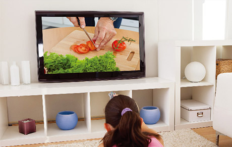 A girl watching a cooking instructional on her living room TV that's on a floor shelf