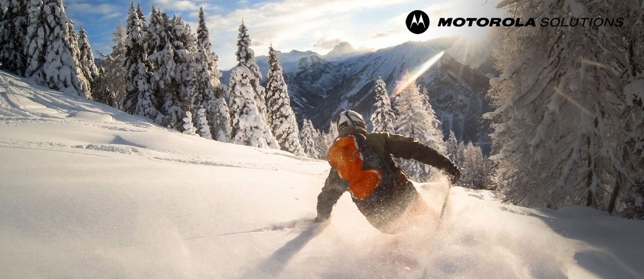  A man skiing down a slope, with trees and mountains covered in snow in the background  