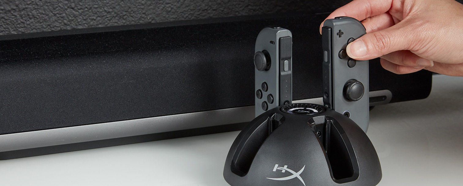 Two Joy-Con plugged into the HyperX ChargePlay Quad next to a sound bar and hand grabbing one of the Joy-Con