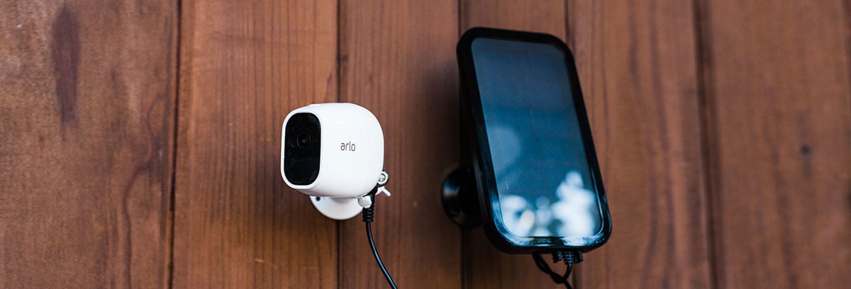 Arlo Pro 2 Installed on a Wooden Wall Next to a Mounted Smartphone