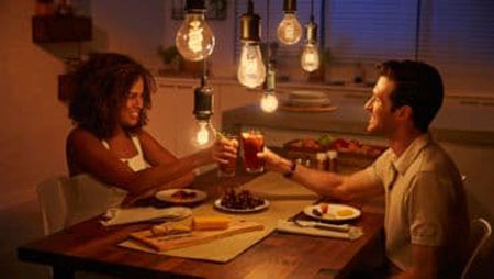 a man and a woman having dinner with smart bulbs above their head