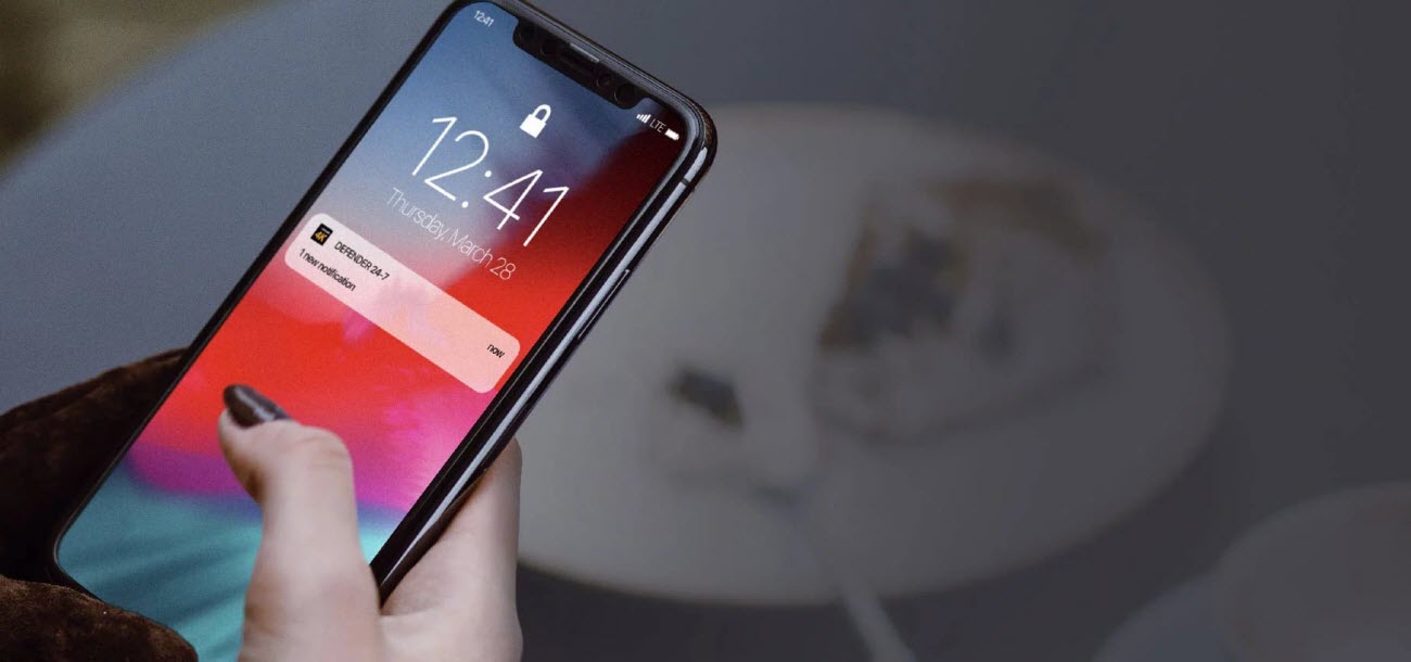 a hand holding an iPhone X showing notifications from the defender 24-7 app
